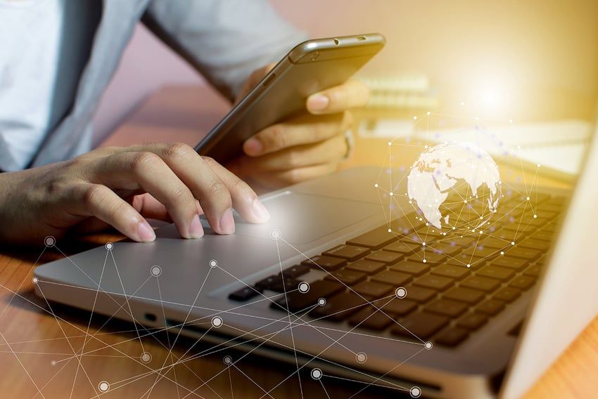 Global Scale Image of individual using a laptop and mobile device with overlay graphic of the globe