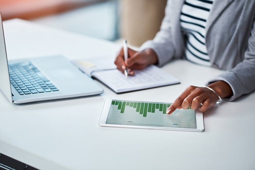 Persona escribiendo información financiera mirando un gráfico y el portátil frente a ella