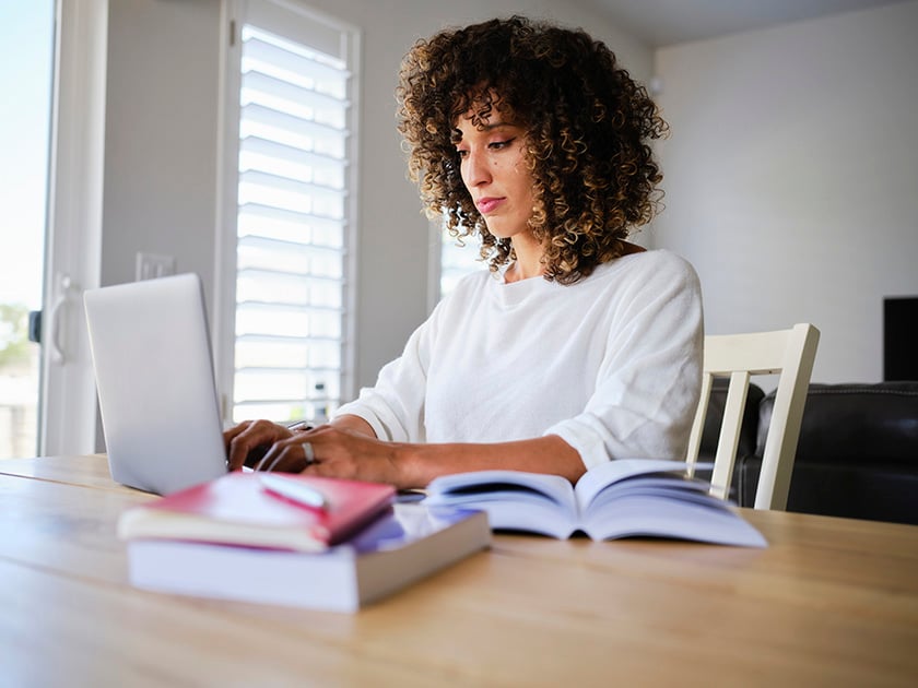 Estudiante con libros académicos abiertos mirando un portátil