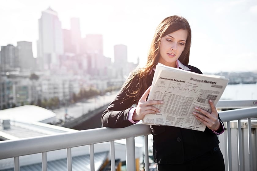 Mujer leyendo el periódico apoyada en una valla